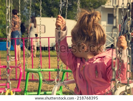 vintage portrait of Sad little girl sitting on swing in a park, looks for her mum
