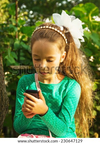 Girl sits in the park and plays with cell phone