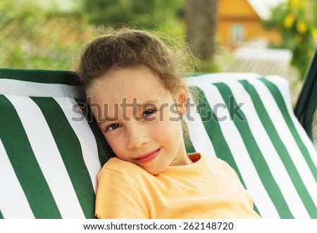 Beautiful sad school girl is resting against green of summer park.