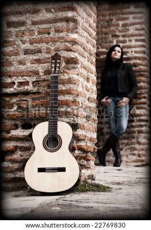 Young female guitar performer posing in an old wall.