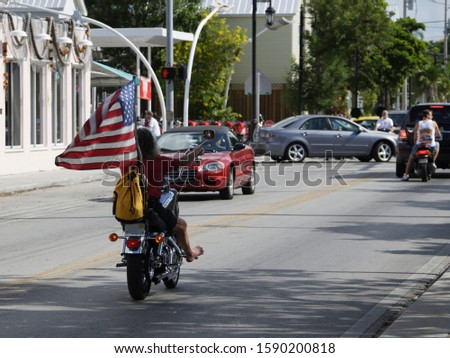 Barefoot Biker riding on street with American flag, Key West, Florida, United States