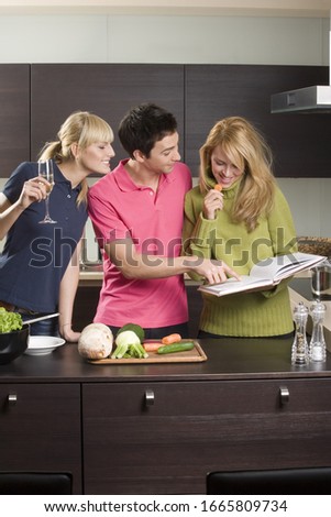 Three friends in kitchen with cookbook and vegetables