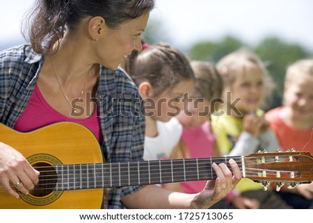 Kindergarten teacher playing guitar to class in a wood kindergarten