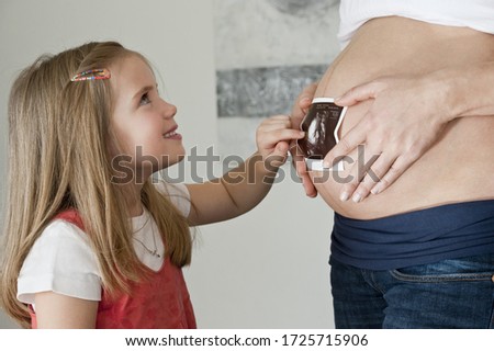 Pregnant mid adult mother and daughter holding ultrasound scan on belly