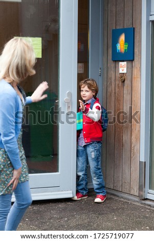 Young boy waving goodbye to mother at school entrance