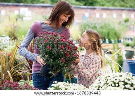 Mother and daughter choosing plants in garden center store holding potted plant