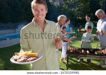 Man with food at multi-generation family barbecue in garden at home