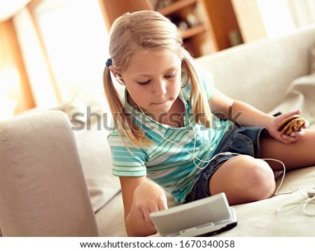 Girl on home sofa listening to music and playing video game using MP3 player and console