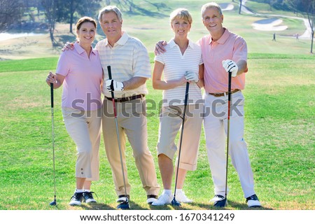 Portrait of smiling mature couple with friends on golf course together