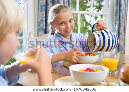 Girl pouring milk on cereal at family breakfast table at camera