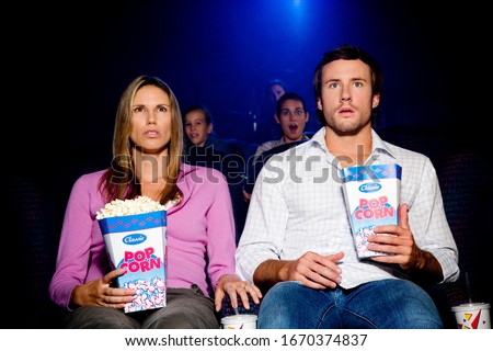 Couple eating popcorn at cinema watching scary movie