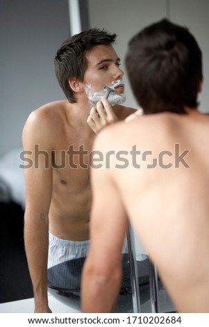 Young man shaving in the mirror
