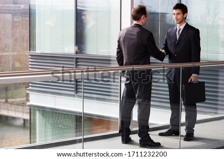Two businessmen shaking hands in an office hallway