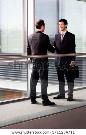 Two businessmen shaking hands in an office hallway