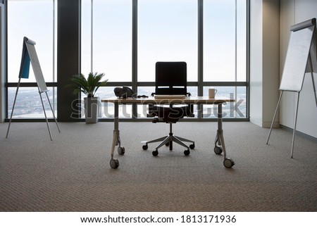 A wide view of a desk and chair in office in front of whiteboard and window.