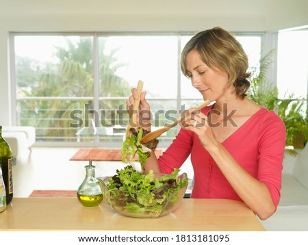 A woman mixing lettuce salad in a glass bowl using wooden spoons.