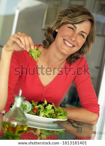 Tilted shot of a happy woman at the dining table eating a lettuce salad.