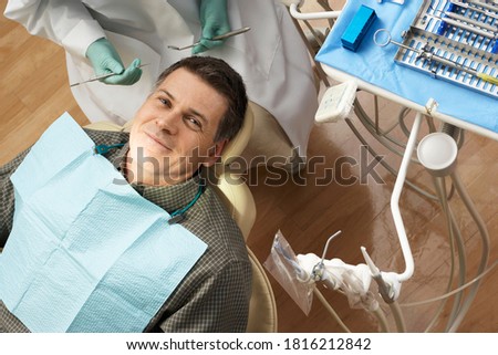 Top view of a man in a dental chair smiling at the camera while being examined by a female dentist.