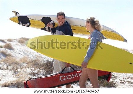 Three quarter length profile shot of a young happy couple carrying yellow surfboards on beach.