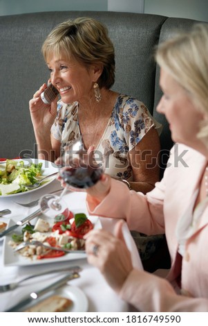Profile shot of two senior women dining in restaurant with focus on woman using mobile phone.