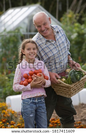 Old man with a basket full of vegetables standing with a girl holding tomatoes.