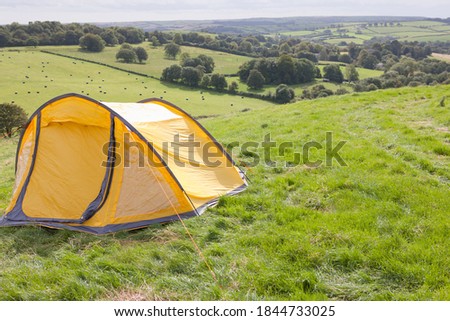Yellow tent set up on a open grassy field on a sunny day.