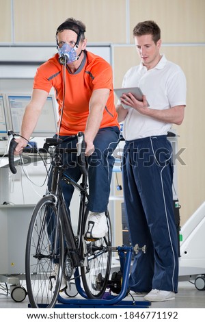 A sports scientist monitoring a runner exercising with a mask on a treadmill in laboratory
