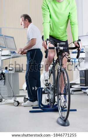 A sports scientist monitoring exercising data of a cyclist working out on an exercise bike