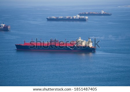 Side view of a natural gas cargo ships travelling at the sea with container ships in the background.