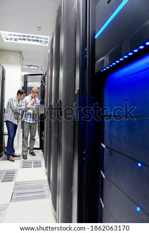 Vertical shot of two technicians looking at the laptop while checking the server