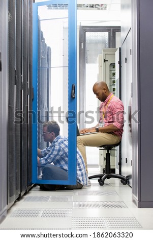 Vertical shot of two technicians sitting in the data center and checking the server