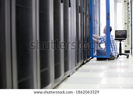 Wide shot of a technician checking the server while sitting on the floor of a data center