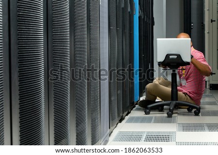 Wide shot of a technician with laptop kept on a moving chair checking the server in the data center