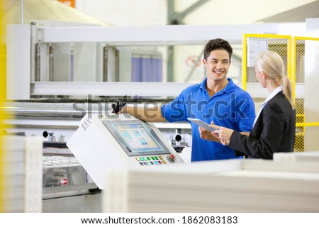 Manager holding a digital tablet and talking to a smiling worker on the production line on the factory floor