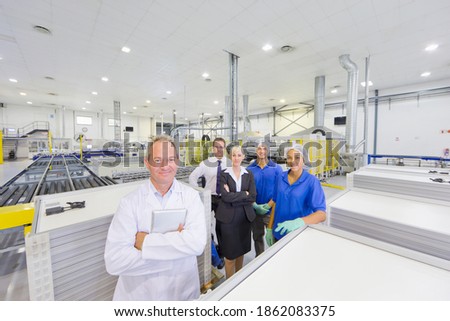 Wide shot of factory owners and employees standing together on the floor of a solar panel factory