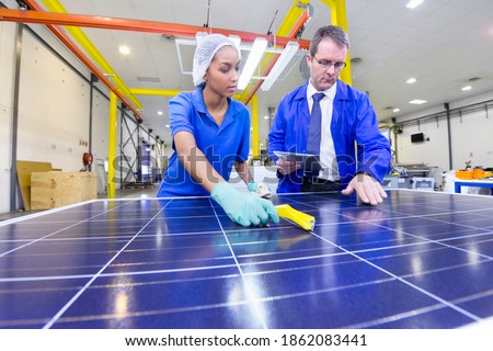 Supervisor examining new solar panel while the technician is cleaning it in the factory