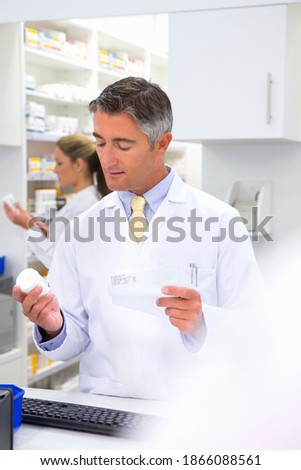 Male pharmacist reading the label on a medicine pot at the pharmacy counter.