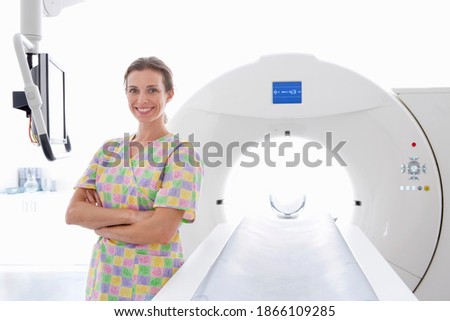 A smiling nurse standing beside the CT scanning machine in the hospital