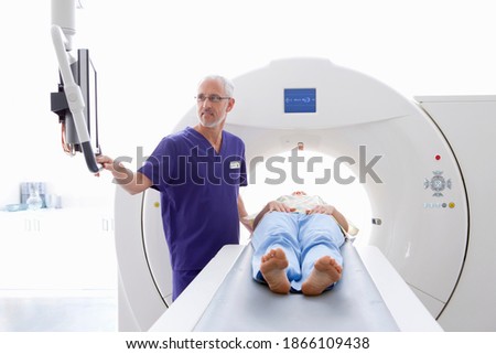 A doctor is checking the reports of a patient displayed on the monitor in the CT scanning room while the patient is laying on the machine