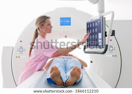 A nurse reviewing the digital scan of a patient displayed on the monitor in the hospital while the patient is laying on the CT scanner