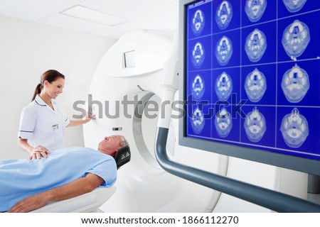 Nurse comforting a patient at the CT scanner behind the digital brain scan monitor in the hospital