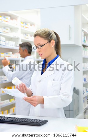 Vertical shot of a female pharmacist reading the label on a medicine pot at the pharmacy counter.