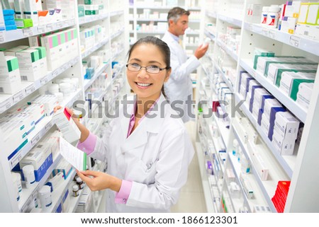 Pharmacist with a prescription and medicine box standing in a pharmacy and smiling at the camera.