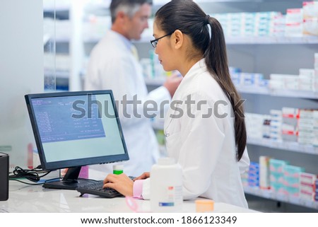 Medium shot of a female pharmacist working on a computer at a pharmacy counter.