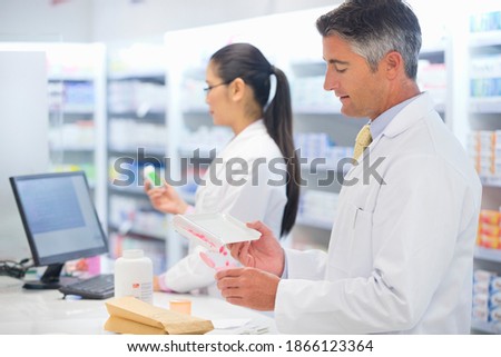 Side view of a male pharmacist counting and dispensing medications at a pharmacy counter.