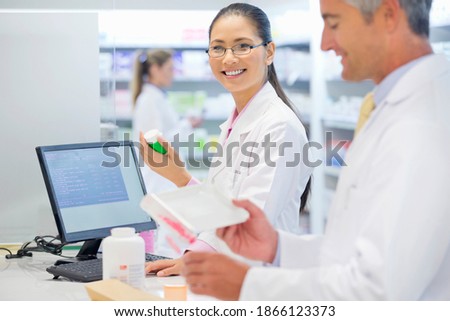 Portrait shot of a female pharmacist inspecting medicines at a pharmacy counter and smiling at the camera.
