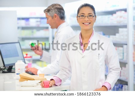 Female pharmacist counting medication at a pharmacy counter and smiling at the camera.