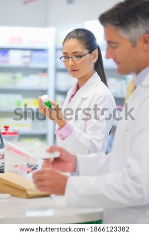 Vertical shot of pharmacists in aprons inspecting medicines at a pharmacy counter.