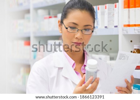 Female pharmacist with a prescription reading the label on a medication pot next to a pharmacy shelf.