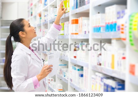 Side view of a pharmacist with a prescription looking for medication on a pharmacy shelf.